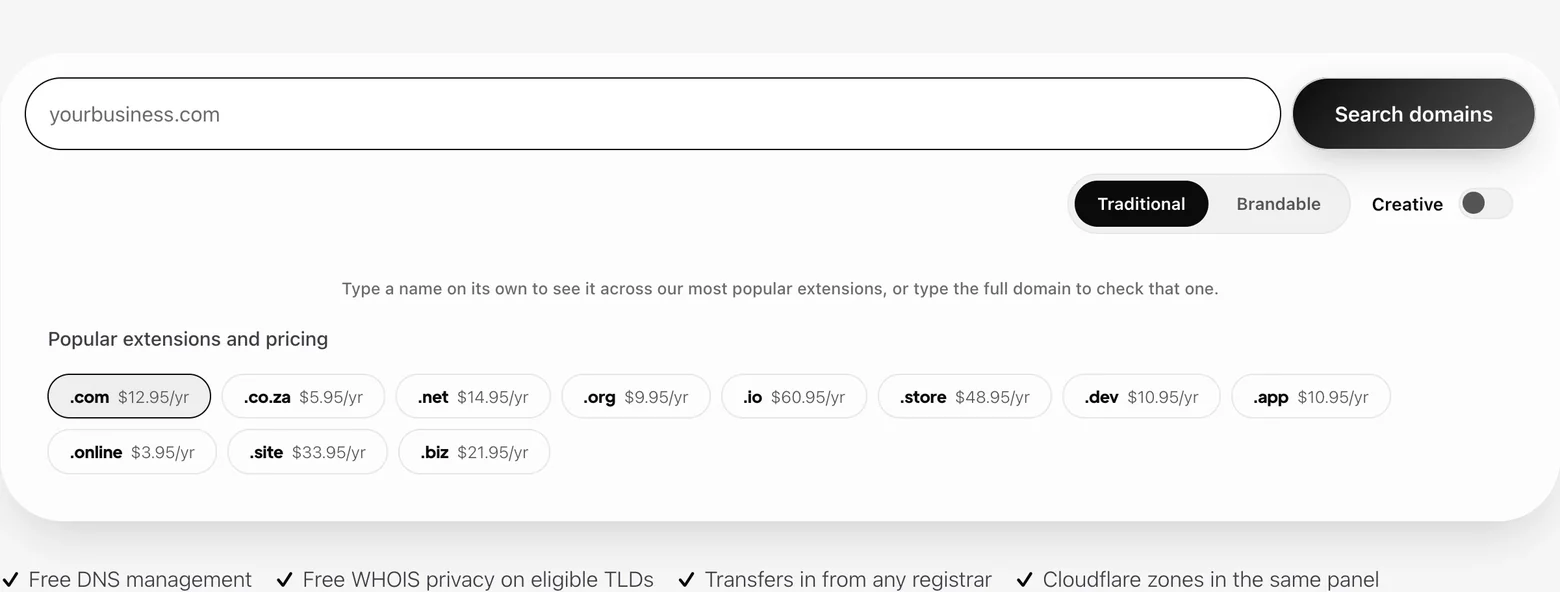 The domain search on the Domains page. A search box reading yourbusiness.com sits beside a Search domains button, with Traditional and Brandable as a pair of buttons and Creative as a separate toggle beneath it. Below the controls, a line reads Type a name on its own to see it across our most popular extensions, or type the full domain to check that one, then a Popular extensions and pricing row shows .com at $12.95 a year, .co.za at $5.95, .net, .org, .io, .store, .dev, .app, .online, .site and .biz, each with its price. A strip underneath lists free DNS management, free WHOIS privacy on eligible TLDS, transfers in from any registrar, and Cloudflare zones in the same panel.