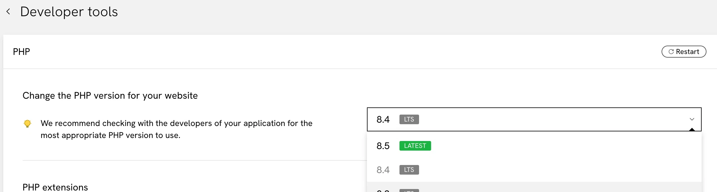 The PHP panel under Developer tools. A Change the PHP version for your website heading sits beside a version dropdown reading 8.4 with an LTS tag, and the list is open showing 8.5 tagged LATEST, 8.4 tagged LTS, 8.3 tagged LTS and 7.4 below them. A yellow hint above the dropdown recommends checking with the developers of your application for the most appropriate version, and a Restart button sits in the top right of the panel.